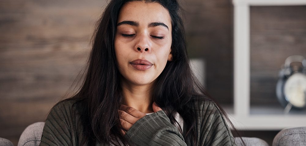 Mulher com os olhos fechados em casa passando por crise de ansiedade.