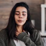 Mulher com os olhos fechados em casa passando por crise de ansiedade.