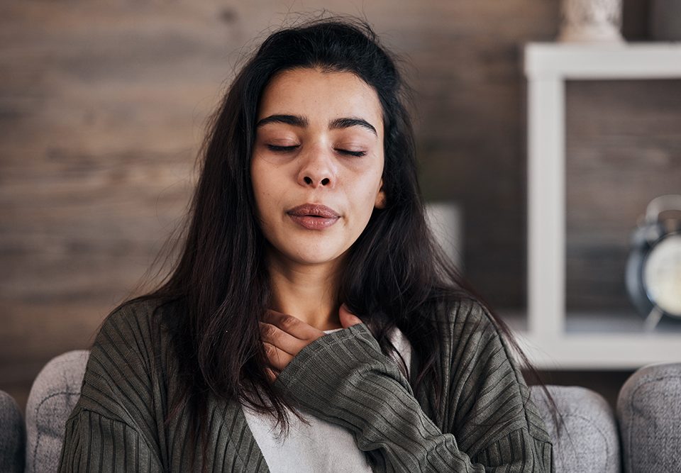 Mulher com os olhos fechados em casa passando por crise de ansiedade.