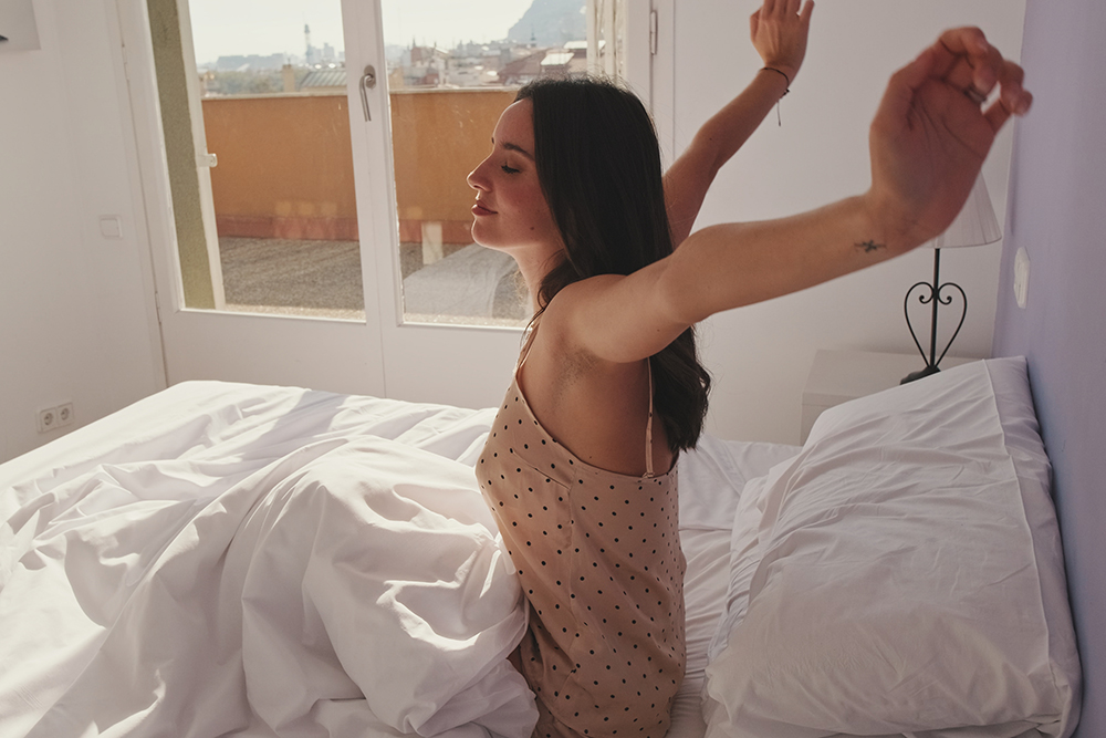 Jovem mulher acorda e se alonga em sua cama