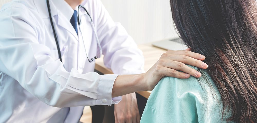 Médico amigável consolando uma paciente e usando a mão no ombro para ajudá-la a relaxar no consultório durante a recepção