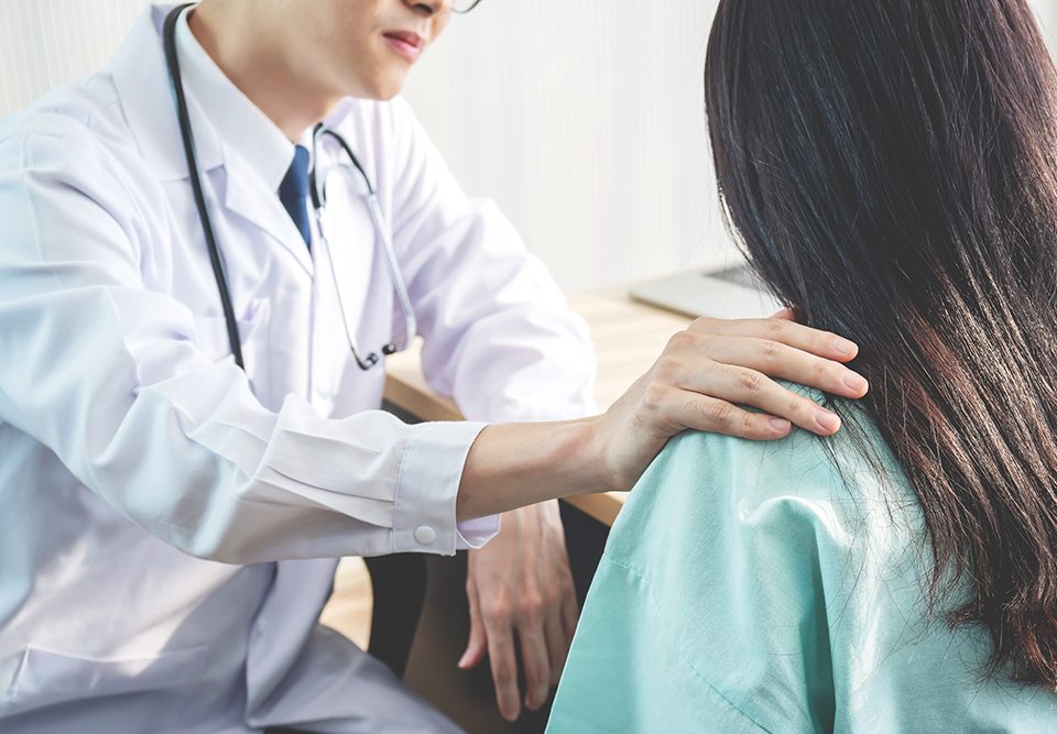 Médico amigável consolando uma paciente e usando a mão no ombro para ajudá-la a relaxar no consultório durante a recepção