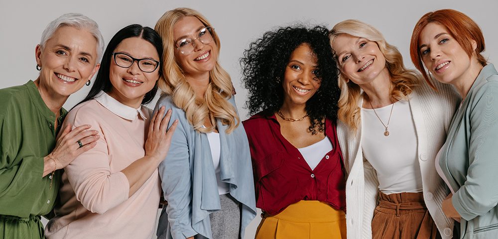 Grupo multiétnico de belas mulheres maduras se unindo e sorrindo contra fundo cinza
