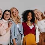 Grupo multiétnico de belas mulheres maduras se unindo e sorrindo contra fundo cinza