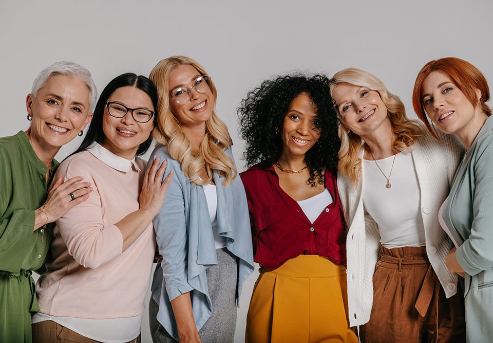 Grupo multiétnico de belas mulheres maduras se unindo e sorrindo contra fundo cinza