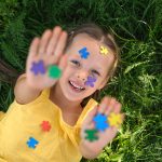 O rosto e as palmas das mãos estão cobertos por quebra-cabeças de papel colorido.