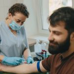 Profissional médico realizando procedimento de coleta de sangue no braço do paciente na clínica.