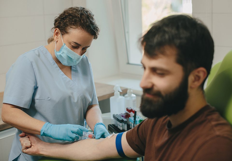 Profissional médico realizando procedimento de coleta de sangue no braço do paciente na clínica.