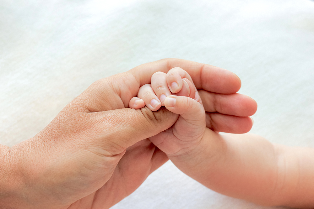 Um bebê recém-nascido segura delicadamente o polegar da mãe