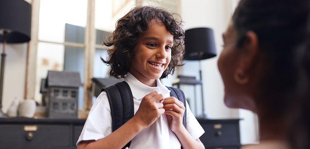 Menino sorrindo para a mãe enquanto se prepara para a escola.
