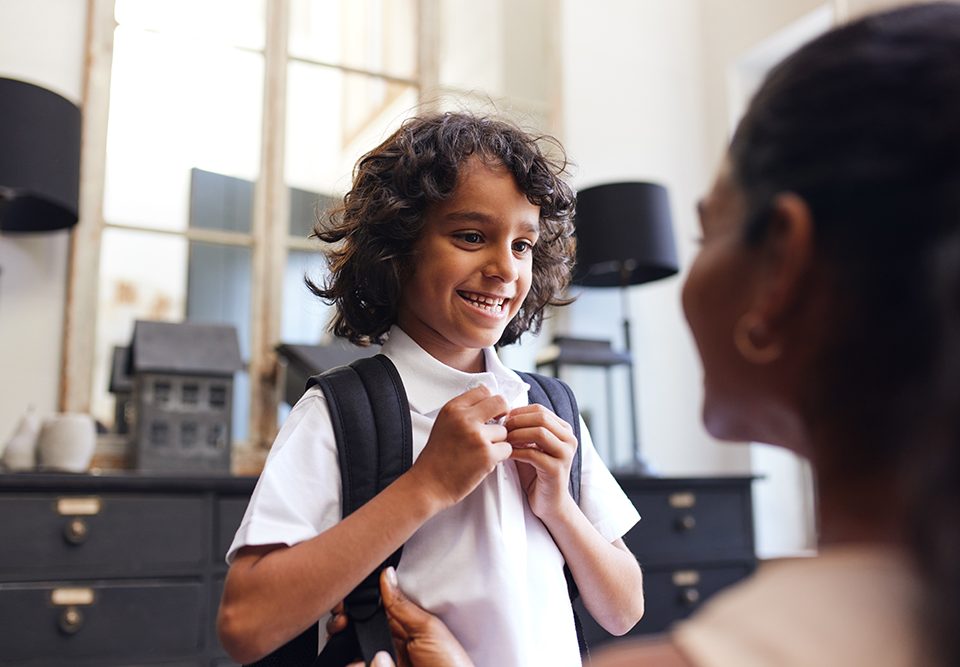 Menino sorrindo para a mãe enquanto se prepara para a escola.