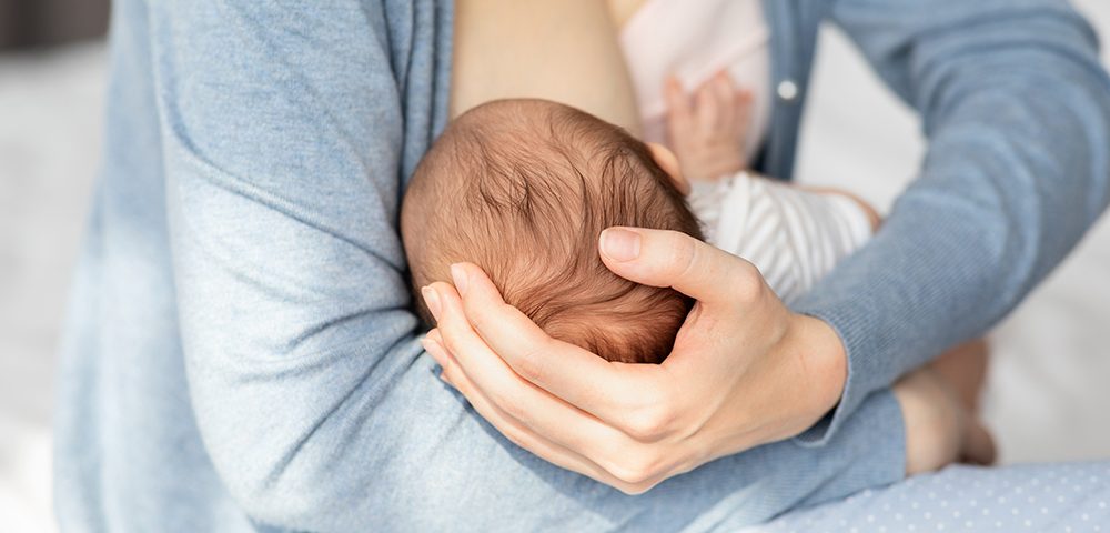 Mulher amamentando bebê recém-nascido em casa.