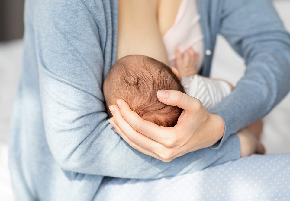 Mulher amamentando bebê recém-nascido em casa.